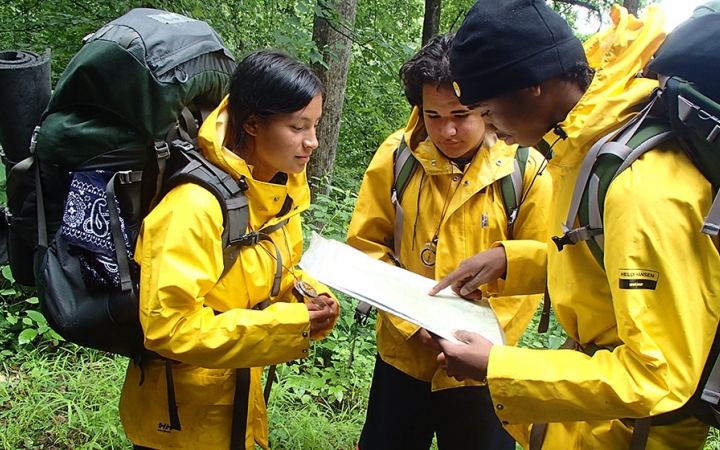 Three students wearing rain jackets and backpacks examine a map.